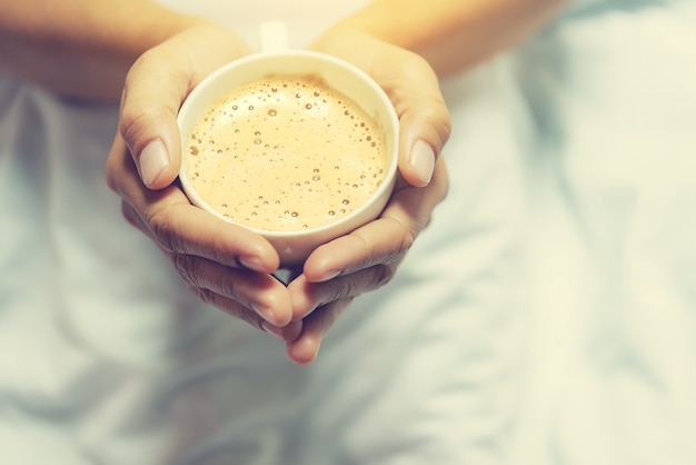 Il concetto dell&#39;amante del caffè delle mani tiene il caffè di mattina sul fondo del letto della sfuocatura