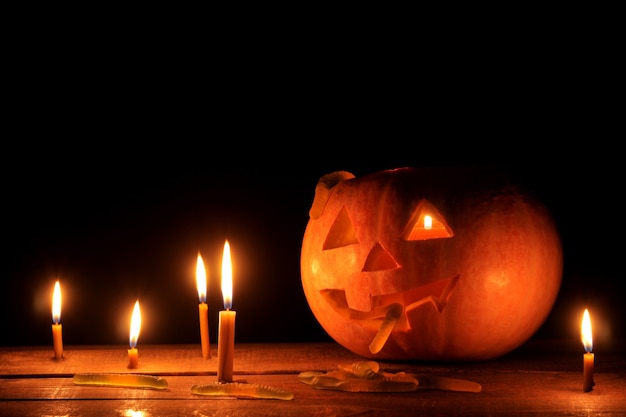 Il concetto della festa di Halloween. Testa di zucca di Halloween con candele dentro e intorno su un tavolo di legno su sfondo nero