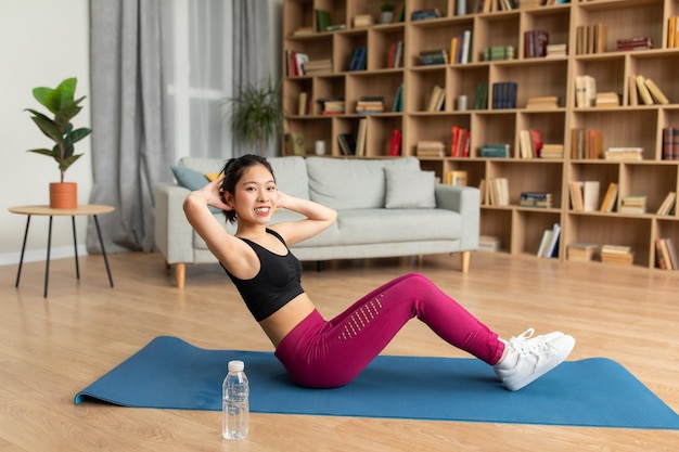 Il concetto di allenamento a casa in forma una signora asiatica che si esercita e fa addominali scricchiolii sdraiati sul tappetino da yoga dentro