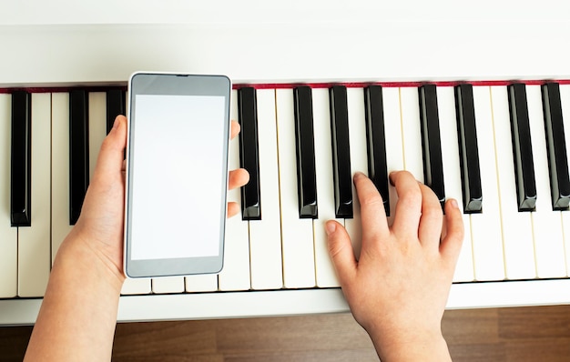 Il concetto di apprendimento del pianoforte online Una mano suona sulla tastiera l'altra tiene lo smartphone Spazio per la copia del fuoco selettivo del primo piano