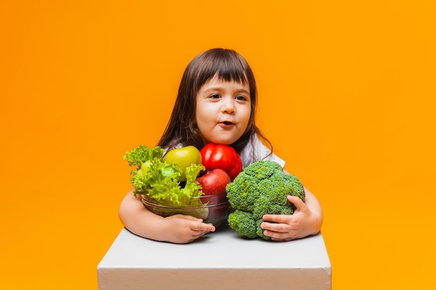 Il concetto di cibo biologico bambina in possesso di un cesto di frutta e verdura su sfondo giallo Alimenti per bambini sani