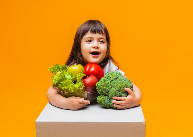 Il concetto di cibo biologico bambina in possesso di un cesto di frutta e verdura su sfondo giallo Alimenti per bambini sani