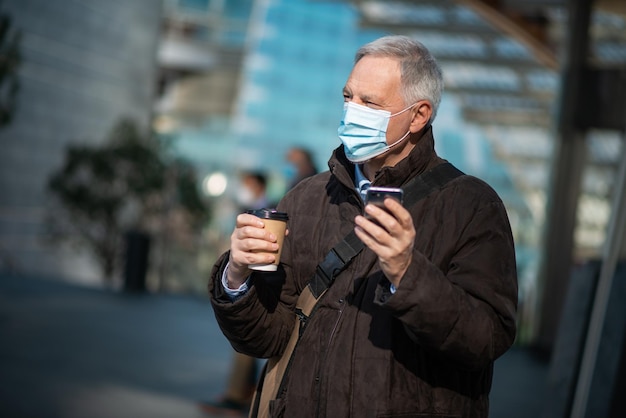 Il concetto di Covid coronavirus mascherava l'uomo anziano usando il suo smartphone all'aperto