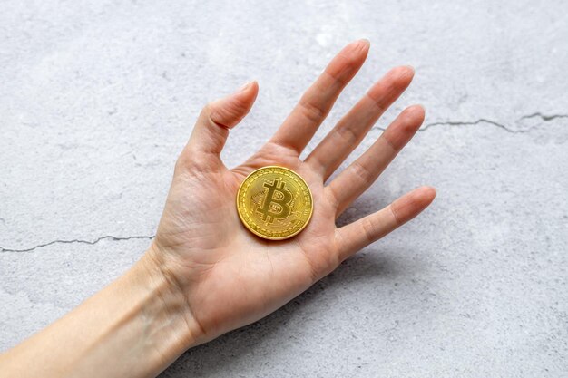 Il concetto di criptovaluta virtuale Bitcoin Money Una mano che tiene una moneta d'oro su sfondo grigio