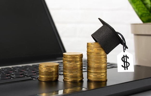 Il concetto di educazione finanziaria Monete d'oro con cappello di laurea in piedi su laptop su desktop