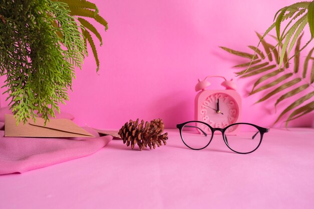 Il concetto di idee di composizione che caratterizzano i prodotti. sfondo rosa decorato con occhiali, orologio, fiori di pino, foglie e stoffa