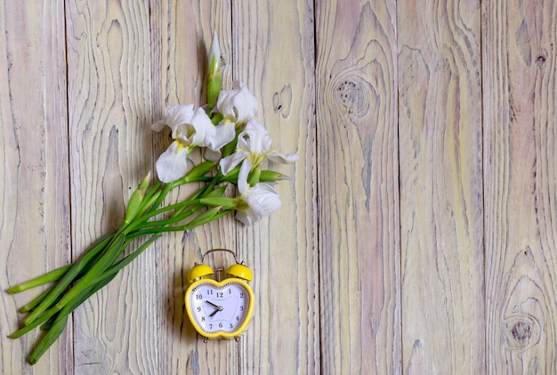 Il concetto di primavera Bouquet di delicate iridi bianche primaverili e orologio giallo su sfondo di legno closeupxDxA