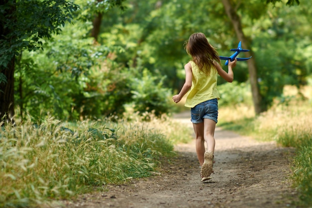 Il concetto di sogni e viaggi. Bambino felice della ragazza che gioca con l'aeroplano del giocattolo di estate sulla natura.