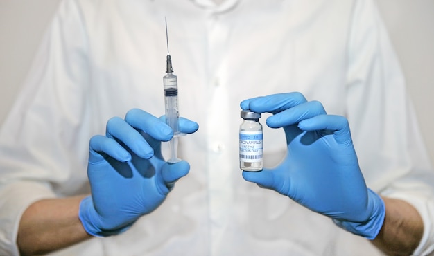 Il concetto di vaccinazione Le mani in guanti blu tengono una siringa medica e un'ampolla