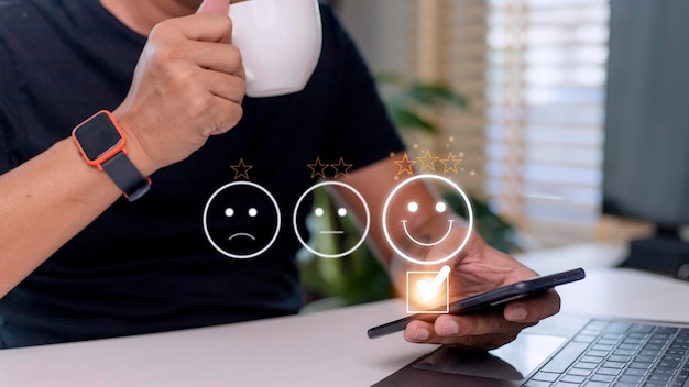 Il concetto di valutazione del servizio clienti che utilizza uno smartphone sta premendo l'emoticon del viso sorridente con soddisfazione sul touch screen virtuale