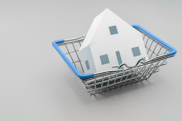 Il concetto di vendita di mutui e affitto di alloggi e immobili Prestito di credito ipotecario Un modello di una casa di carta che giace in un cestino da un negozio su sfondo grigio Spazio di copia