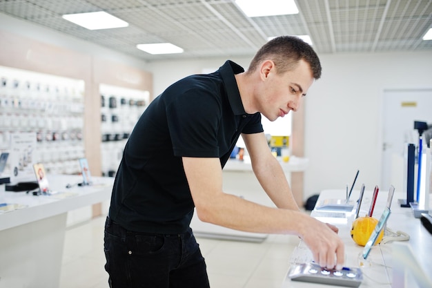 Il consulente professionale del telefono cellulare dell'uomo del venditore nel negozio di tecnologia o nel negozio tiene il nuovo smartphone a portata di mano.