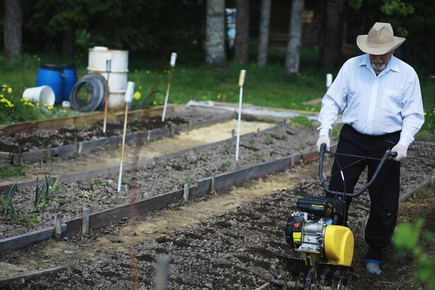 Il contadino sta scavando un giardino Un uomo con una mietitrice ara il giardino Il nonno dai capelli grigi falcia il giardino