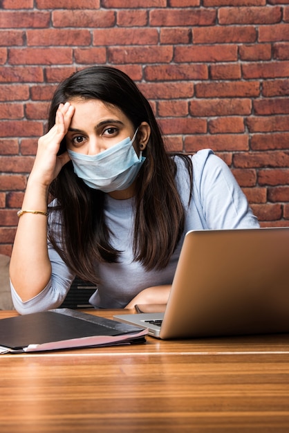 Il coronavirus lavora da casa concetto - quarantena indiana bella donna d'affari, che lavora al laptop indossando una maschera protettiva medica