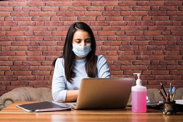 Il coronavirus lavora da casa concetto - quarantena indiana bella donna d'affari, che lavora al laptop indossando una maschera protettiva medica