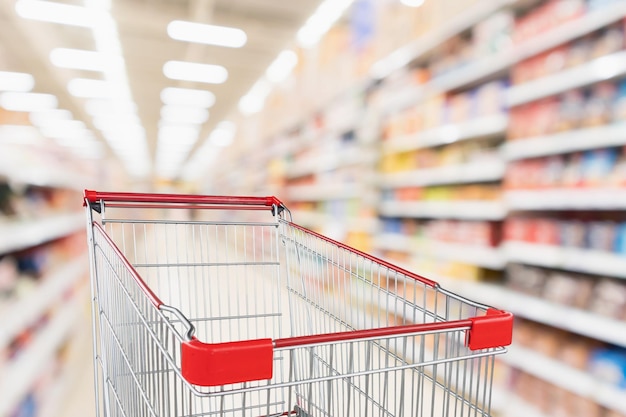 Il corridoio del supermercato ha sfocato lo sfondo con il carrello della spesa rosso vuoto