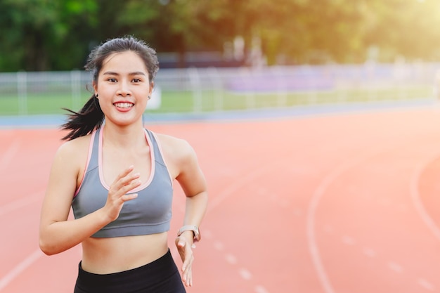 Il corridore asiatico della donna di sport felice si diverte a correre nell'attività sana del campo di atletica all'aperto