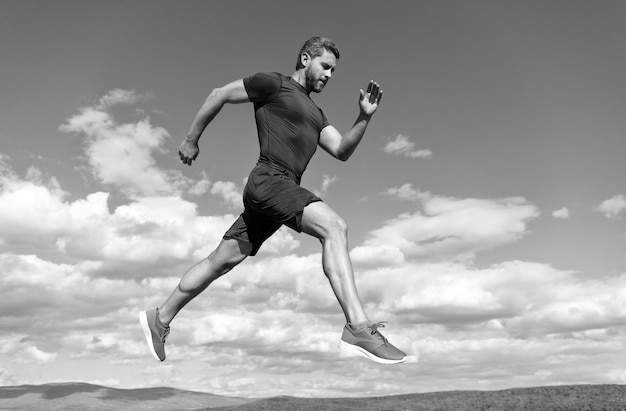 Il corridore dell'uomo dello sportivo corre verso il successo o salta in alto sullo sport del fondo del cielo