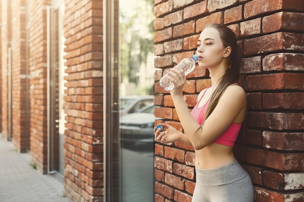 Il corridore della giovane donna sta facendo una pausa, bevendo acqua dopo aver fatto jogging nel centro della città, copia spazio