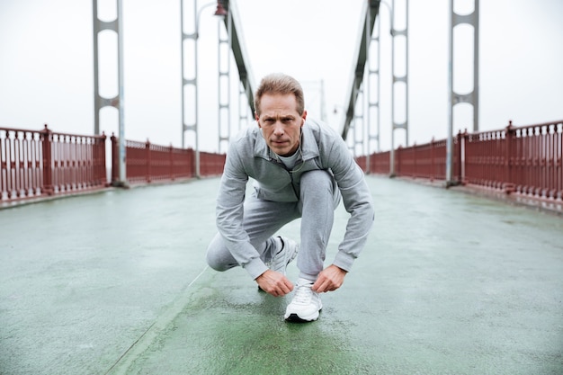 Il corridore in abiti sportivi grigi si prepara sul ponte. Vista frontale