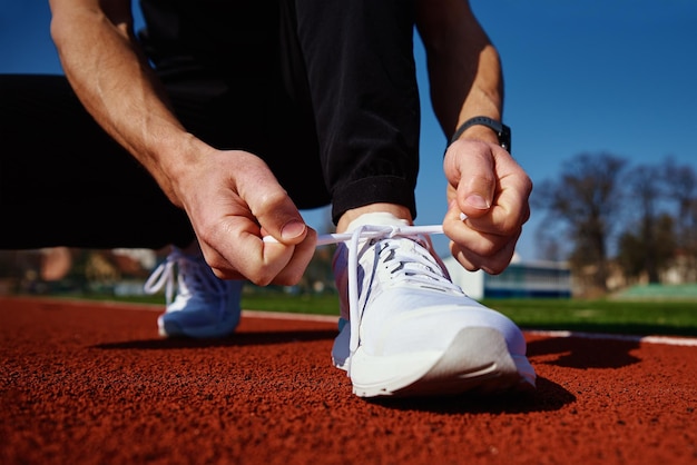 Il corridore maschio in scarpe da ginnastica bianche si prepara per correre sulla pista dello stadio mani maschili che si legano su scarpe da ginnastica sportive