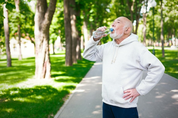 Il corridore maschio senior sta facendo una pausa, bevendo acqua mentre fa jogging nel parco