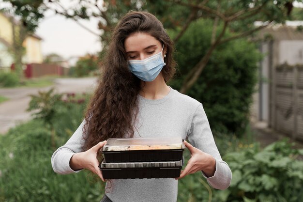 Il corriere della ragazza in maschera medica con 2 scatole di sushi si trova di fronte all'auto. Sushi set in scatola servizio di consegna cibo sano in auto.