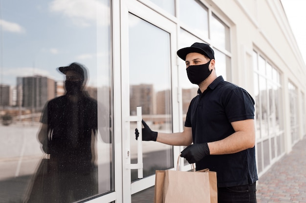 Il corriere in maschera protettiva e guanti medici fornisce cibo da asporto