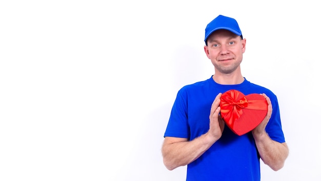Il corriere in uniforme blu tiene una confezione regalo rossa a forma di cuore per San Valentino. Consegna a domicilio di