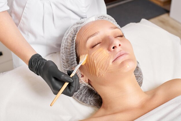 Il cosmetologo applica la maschera al miele sul viso della donna per idratare la pelle del viso nel salone di bellezza spa