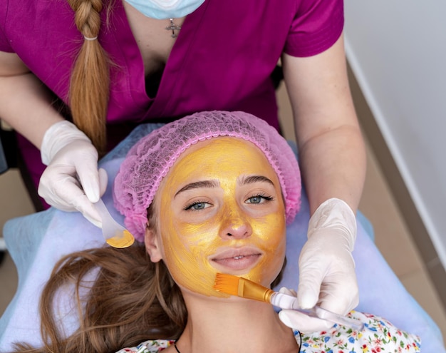 Il cosmetologo applica la maschera di alginato con spatola sul viso della donna. Pelle del viso e trattamento antietà. Cosmetologia e cura professionale della pelle del viso