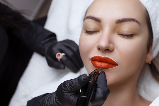 Il cosmetologo fa il trucco permanente sul viso di una donna Lo specialista applica un tatuaggio sul primo piano delle labbra del paziente