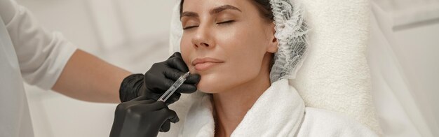 Il cosmetologo fa iniezioni per aumentare le labbra e le rughe della donna nel salone di bellezza