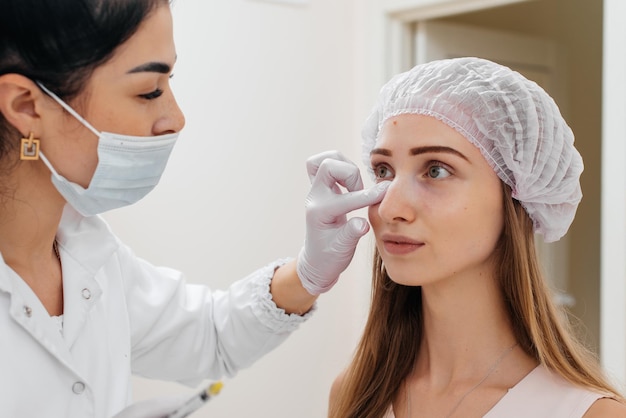 Il cosmetologo pulisce il viso del paziente dopo la procedura di riempimento del solco nasolacrimale e la mesoterapia intorno agli occhi per una giovane e bella ragazza Cosmetologia moderna