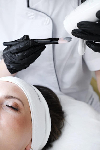 Il cosmetologo spreme una maschera di argilla su un pennello e sta per applicarla sul viso della cliente