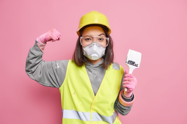 Il costruttore femminile esperto e sicuro di sé alza il braccio mostra che i muscoli tengono il pennello da pittura