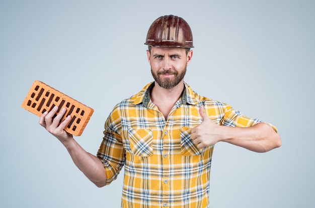 Il costruttore gode del successo. architetto uomo con mattoni. ragazzo indossa l'uniforme da lavoratore. bel costruttore in casco. l'uomo maturo indossa una camicia a scacchi. costruttore o meccanico professionista. ingegnere edile.