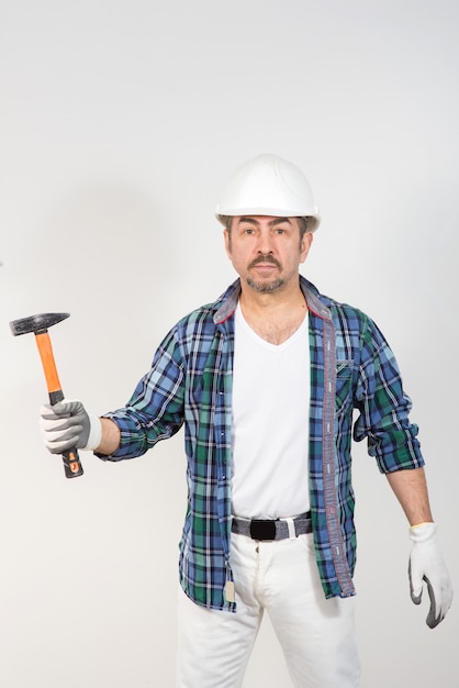 Il costruttore in un casco di sicurezza tiene un martello contro un muro bianco