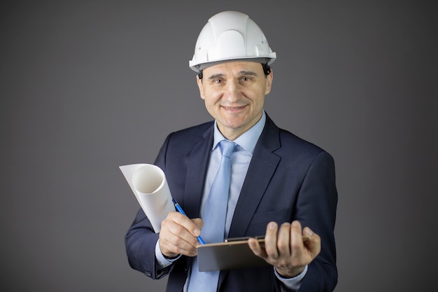 Il costruttore positivo in casco bianco tiene sorridere arrotolato del disegno e della lavagna per appunti