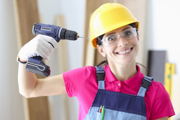 Il costruttore sorridente della donna tiene il trapano vicino alla sua testa