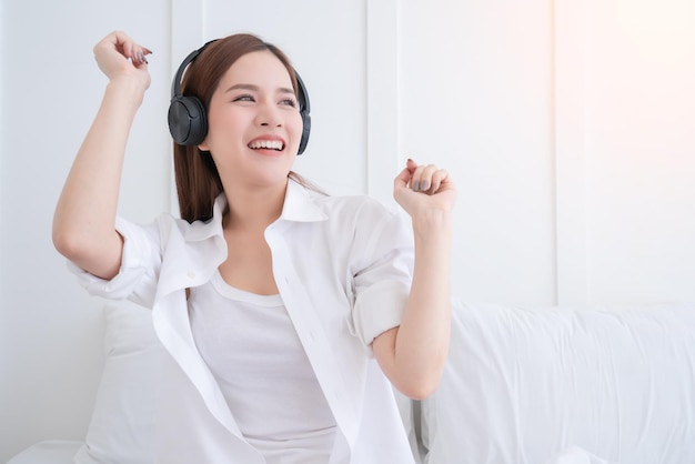 Il costume del vestito bianco della donna asiatica di felicità gode di musica d'ascolto di ballo con lo sfondo della camera da letto delle cuffie