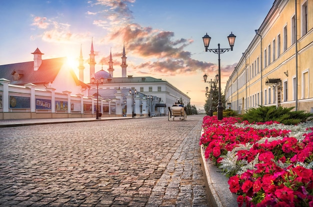 Il Cremlino di Kazan dall'interno si affaccia sulla moschea Kul-Sharif sotto i raggi del sole al tramonto, una carrozza bianca e fiori rossi