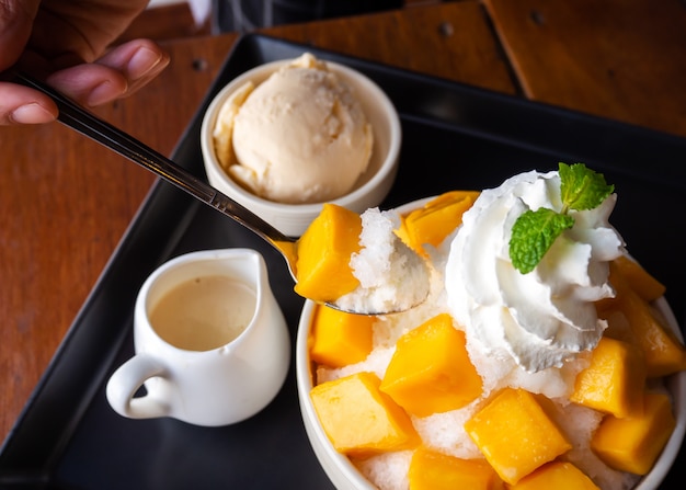 Il cucchiaio di uso della donna prende il dessert tritato del ghiaccio, servito con il mango affettato.