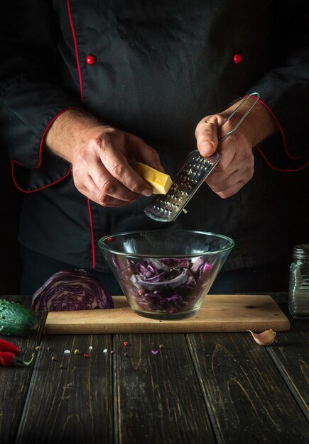 Il cuoco aggiunge il formaggio a un'insalata di cavolo rosso fresco nella cucina di un ristorante Cucinare cibi sani o vegetariani