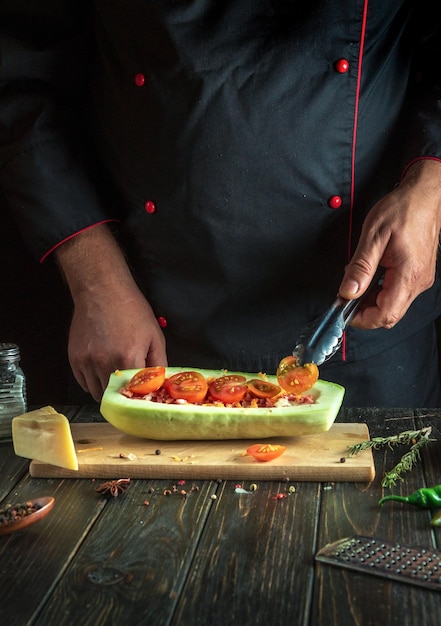 Il cuoco aggiunge un pomodoro alle zucchine Il concetto di cucinare una barca di zucca o un midollo ripieno nazionale nella cucina di un ristorante Spazio libero per il menu