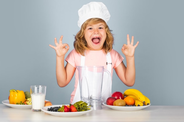 Il cuoco del cuoco del bambino prepara il cibo su sfondo grigio isolato dello studio i bambini che cucinano il ragazzo adolescente con il grembiule un