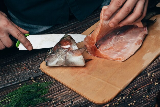 Il cuoco dell'uomo taglia con un coltello per cucinare la trota fresca