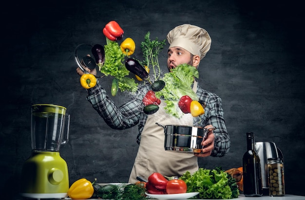 Il cuoco dell'uomo tiene una padella con le verdure che volano nell'aria.