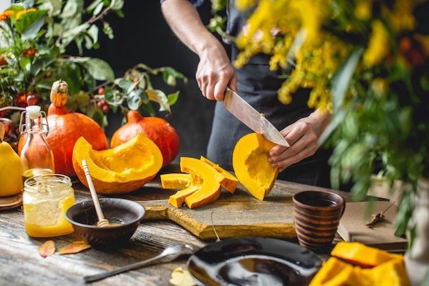 Il cuoco della donna taglia una zucca arancione con un coltello a fette per cuocere