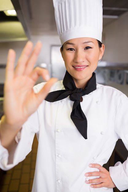 Il cuoco femminile sorridente che gesturing l&#39;approvazione firma dentro la cucina